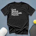 Black t-shirt with "Eat & Sleep & Pickleball & Repeat." text, pickleball, and paddle.