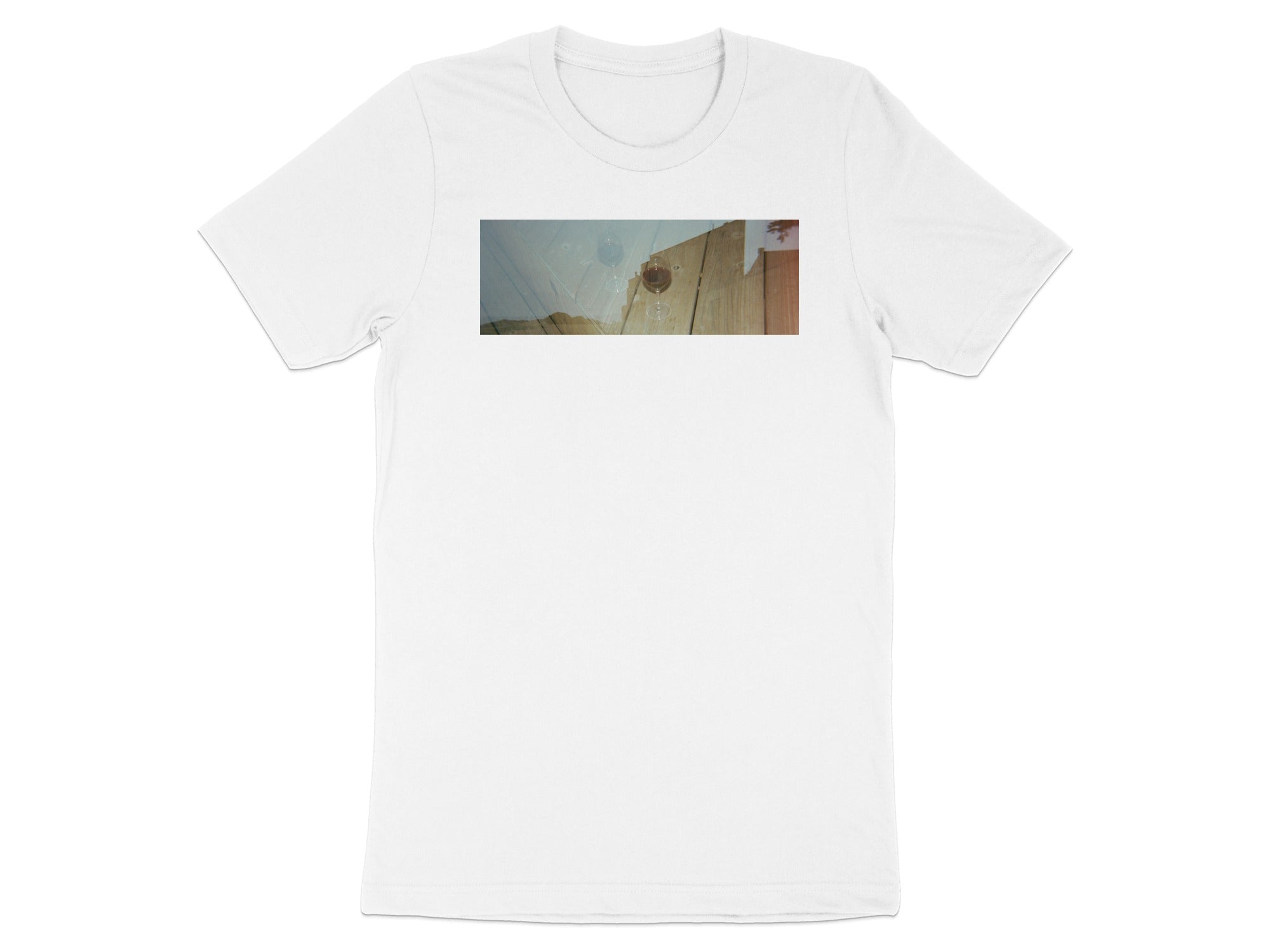 White t-shirt with a double exposure graphic of wine glasses on a wooden table.