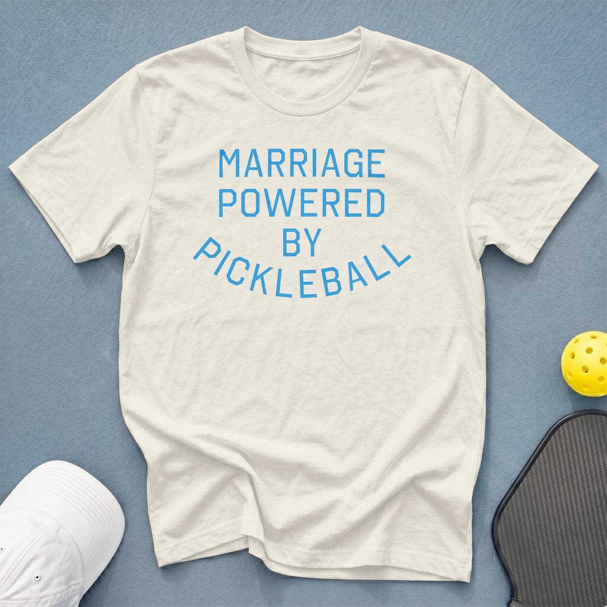 White t-shirt with blue text reading "MARRIAGE POWERED BY PICKLEBALL".