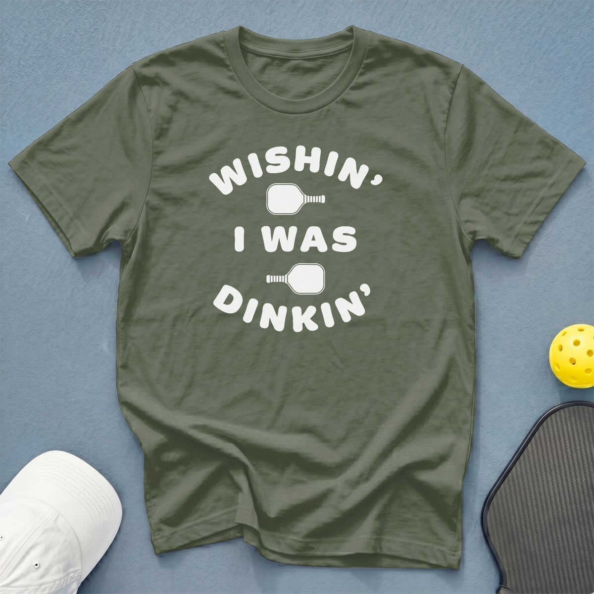 Olive green t-shirt with white text: "Wishin', I Was Dinkin'" and pickleball imagery.