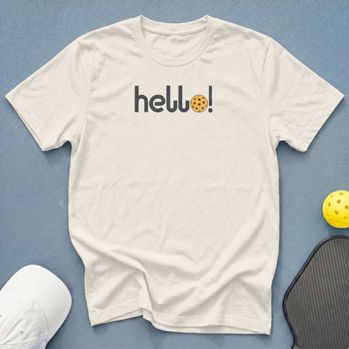 Cream t-shirt with "hello!" graphic featuring a pickleball and pickleball gear.