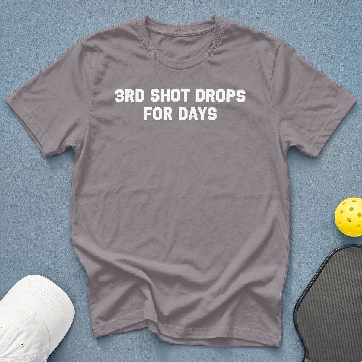 Grape t-shirt with white text "3RD SHOT DROPS FOR DAYS" next to pickleball gear.