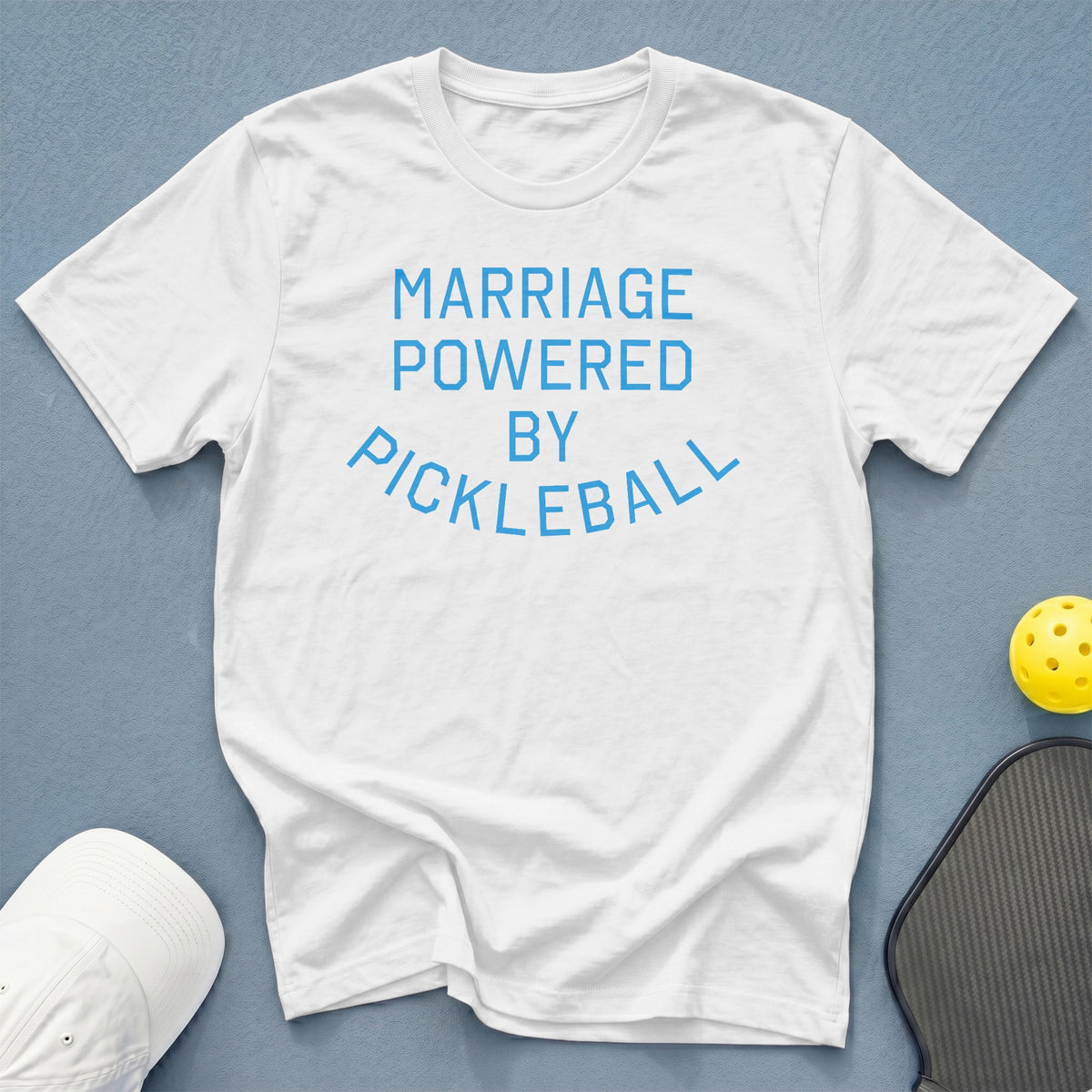 White t-shirt with blue text reading "MARRIAGE POWERED BY PICKLEBALL".