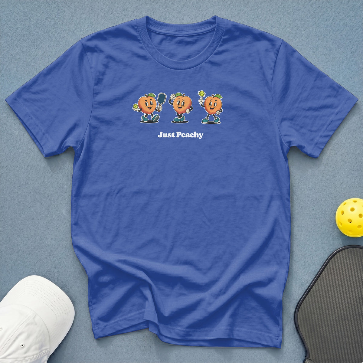 Blue t-shirt with three cartoon peaches playing pickleball and the text "Just Peachy".