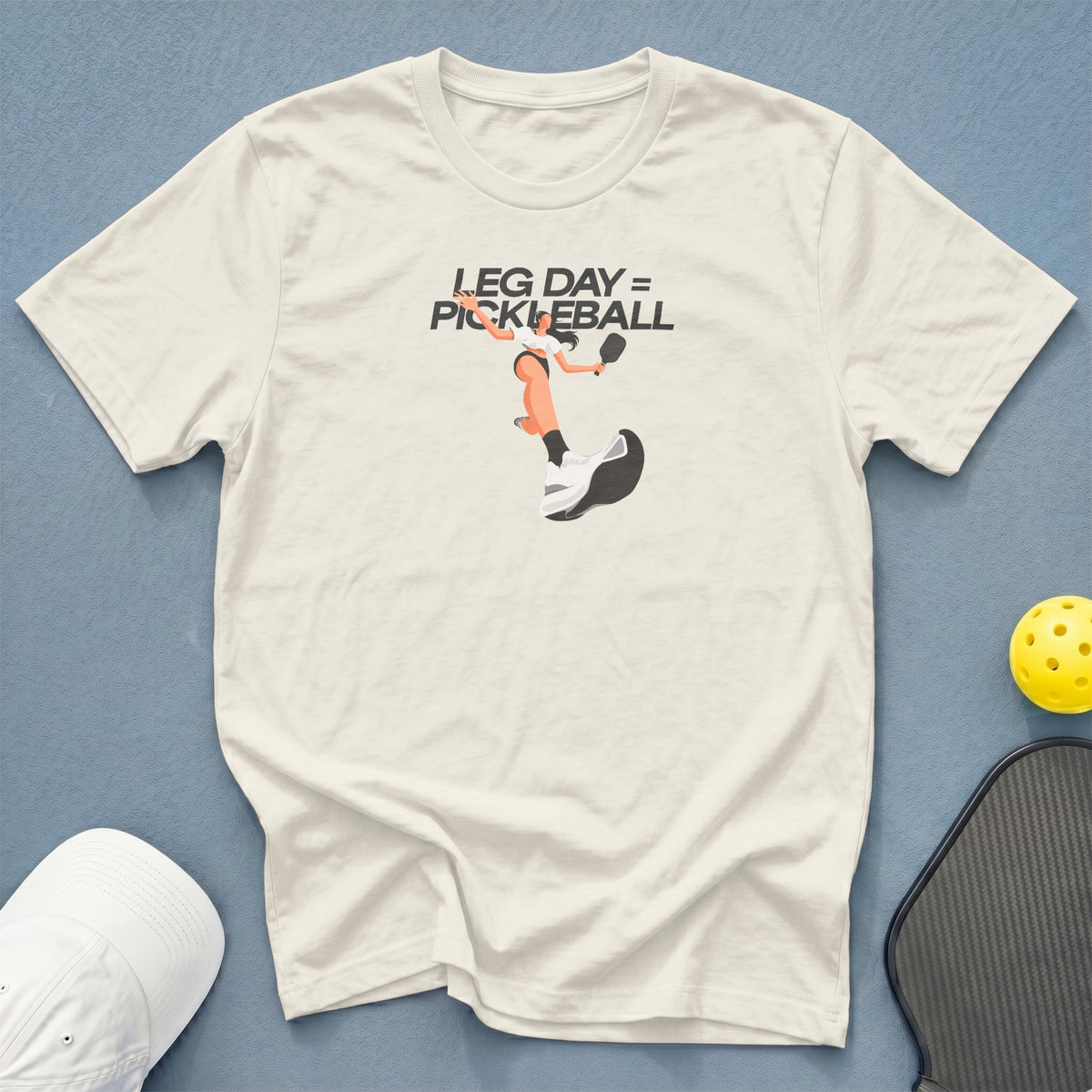 Cream t-shirt with graphic of a pickleball player and text "LEG DAY = PICKLEBALL".