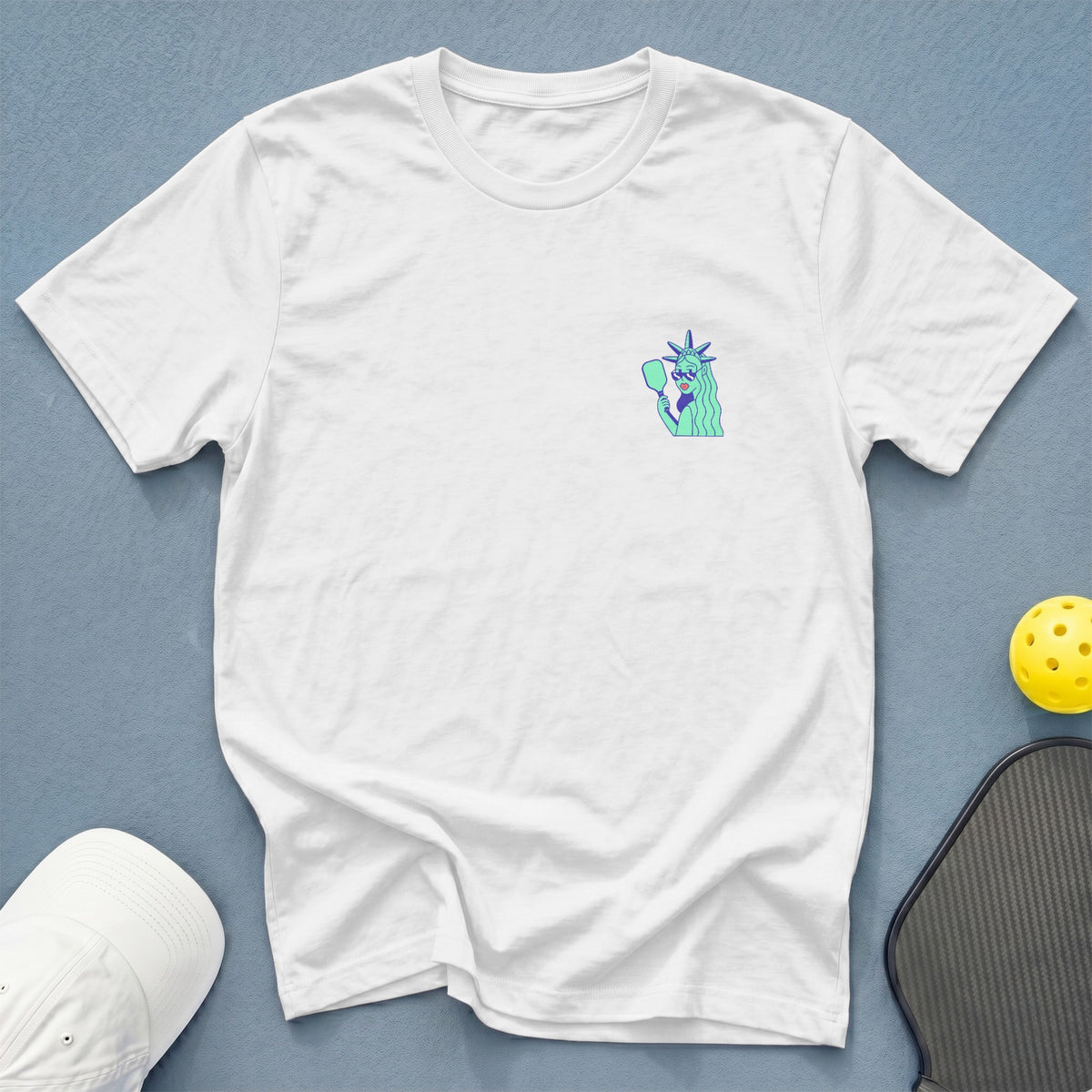White t-shirt with a small Statue of Liberty graphic wearing sunglasses and holding a mirror.
