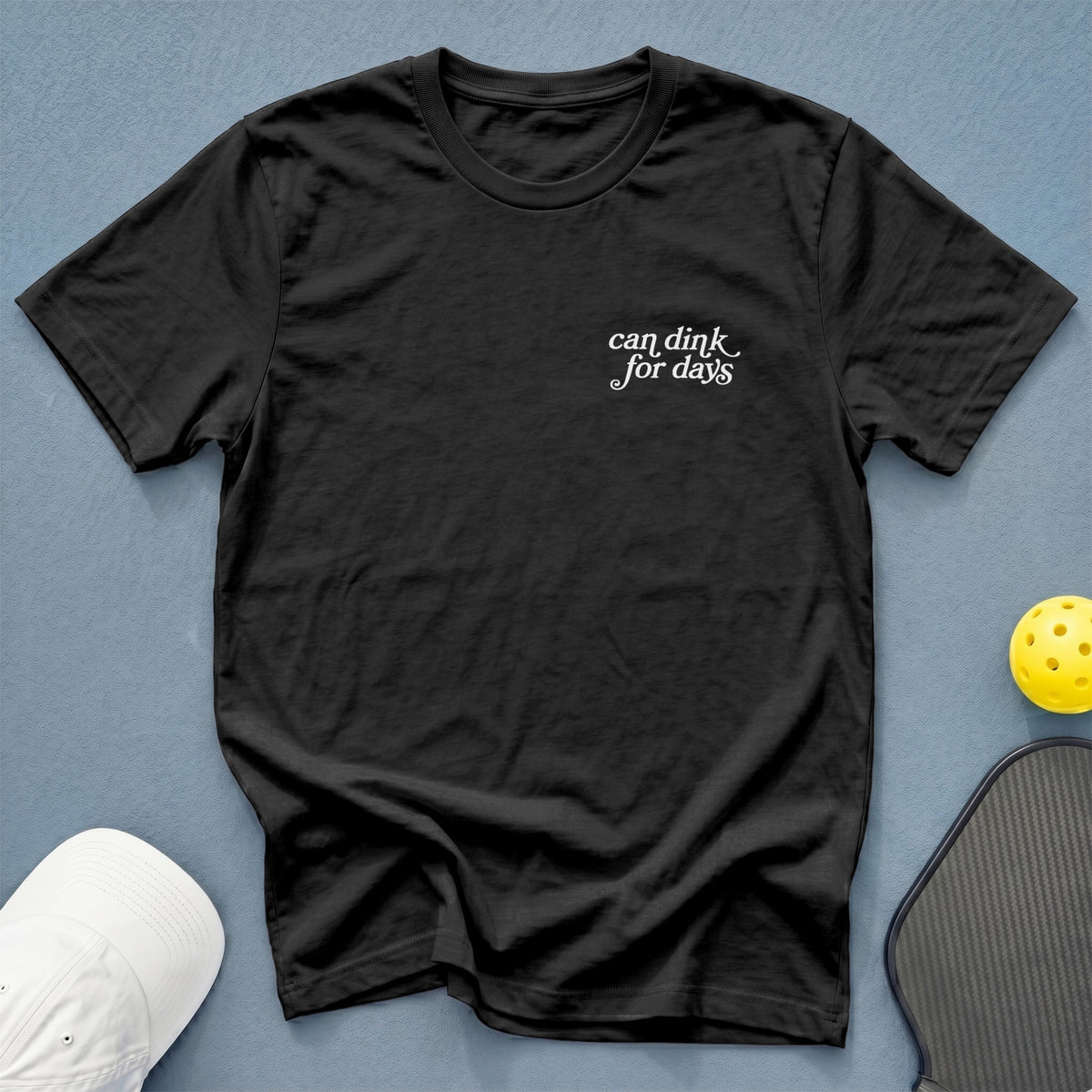 Black t-shirt with white text "can dink for days" and pickleball gear.