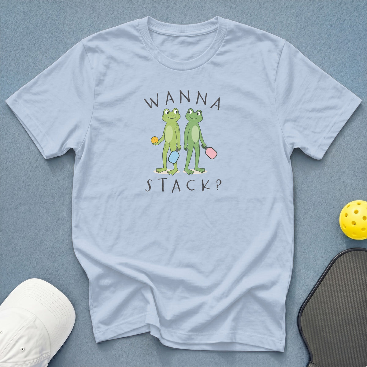 Light blue t-shirt with cartoon frogs playing pickleball and text "WANNA STACK?".