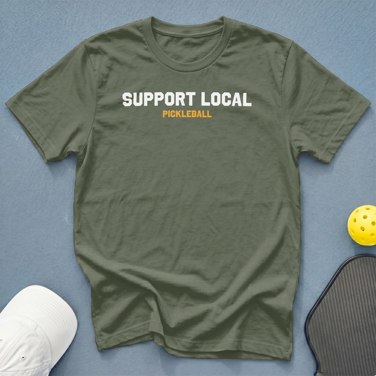 Olive green t-shirt with "SUPPORT LOCAL PICKLEBALL" graphic, pickleball, and hat.