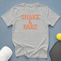 Gray t-shirt with orange "Shake & Bake" text, pickleball paddle, and ball.