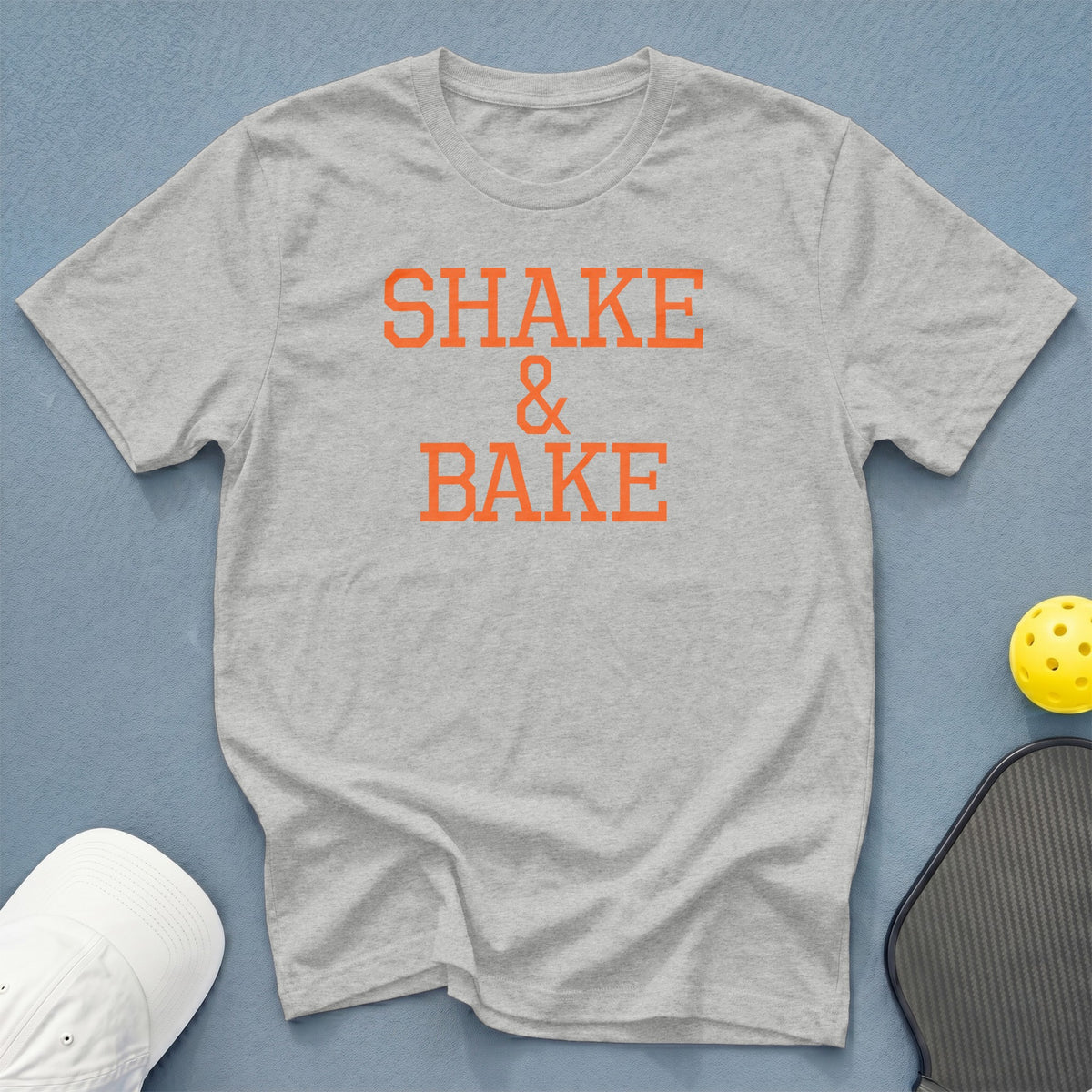 Gray t-shirt with orange "Shake & Bake" text, pickleball paddle, and ball.