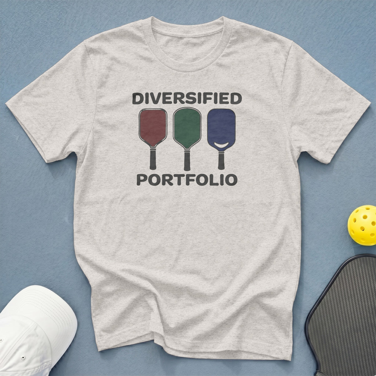 Light grey t-shirt with text "DIVERSIFIED PORTFOLIO" and three colorful pickleball paddles.