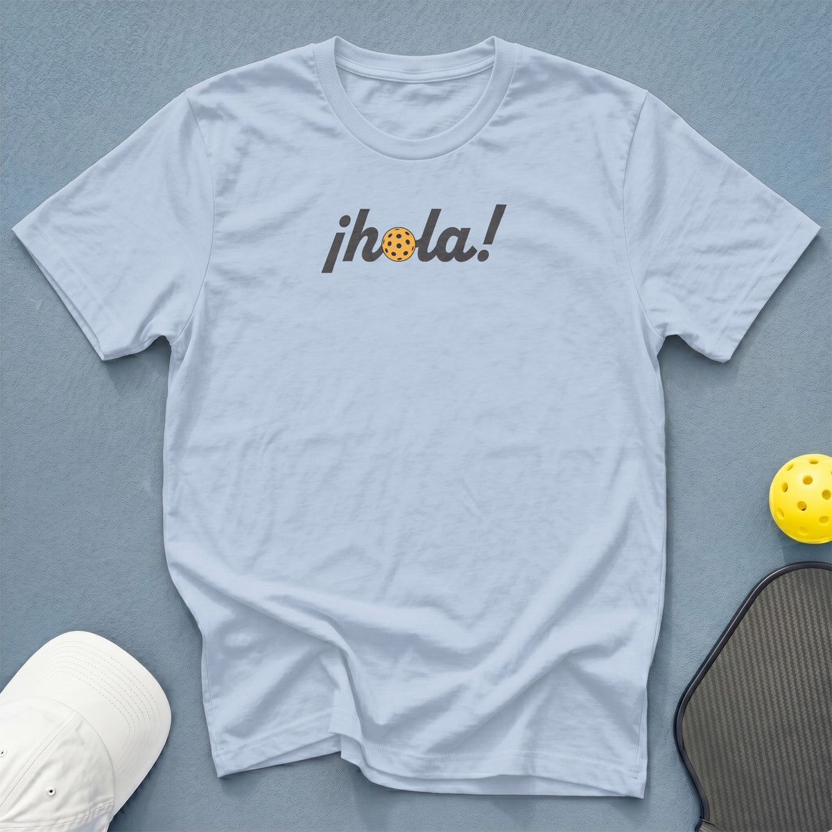 Light blue t-shirt with "¡hola!" text and a pickleball in place of the 'o'.