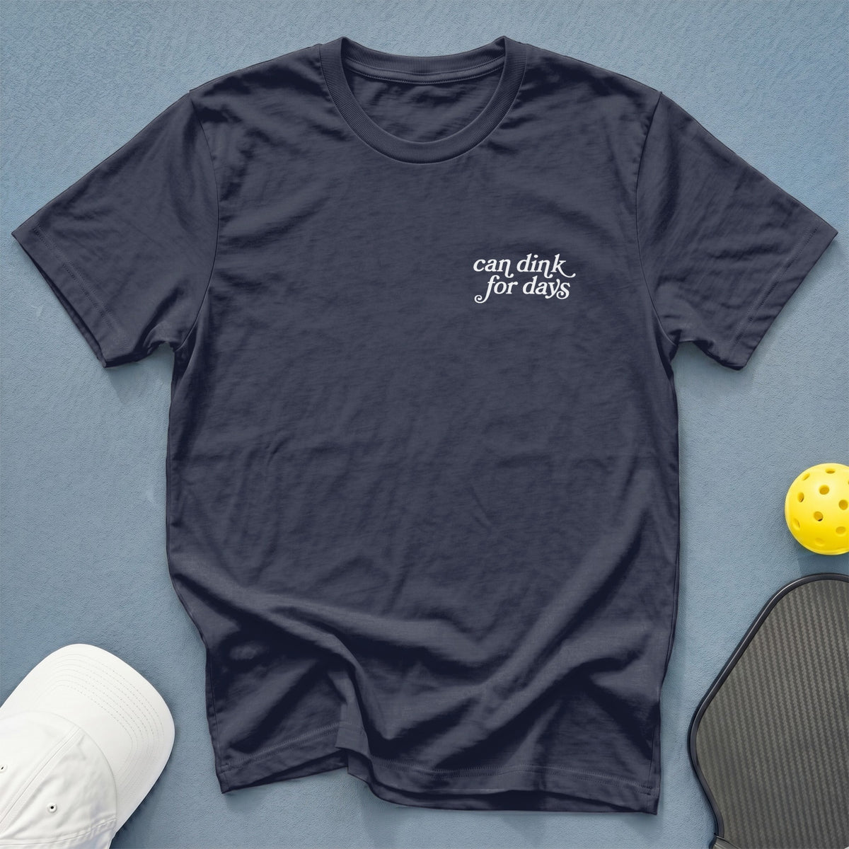 Navy t-shirt with "can dink for days" text, pickleball paddle, ball, and hat.