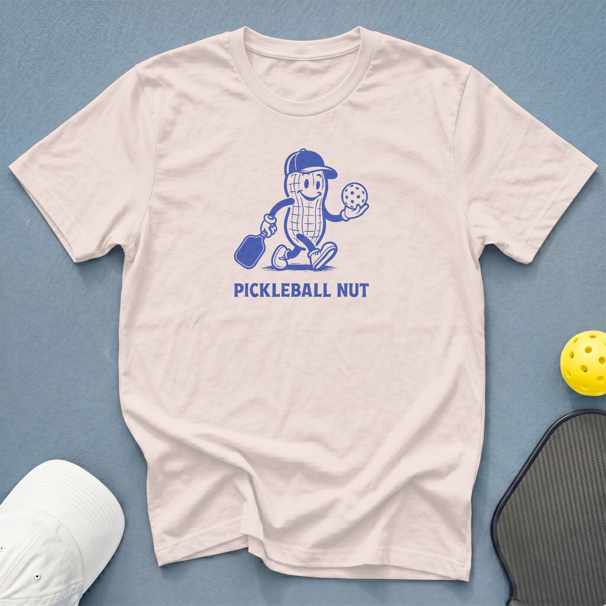 Light pink t-shirt with cartoon peanut holding pickleball paddle and ball, "PICKLEBALL NUT" text.