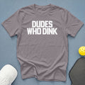 Gray t-shirt with white text "DUDE WHO DINK" next to pickleball gear.