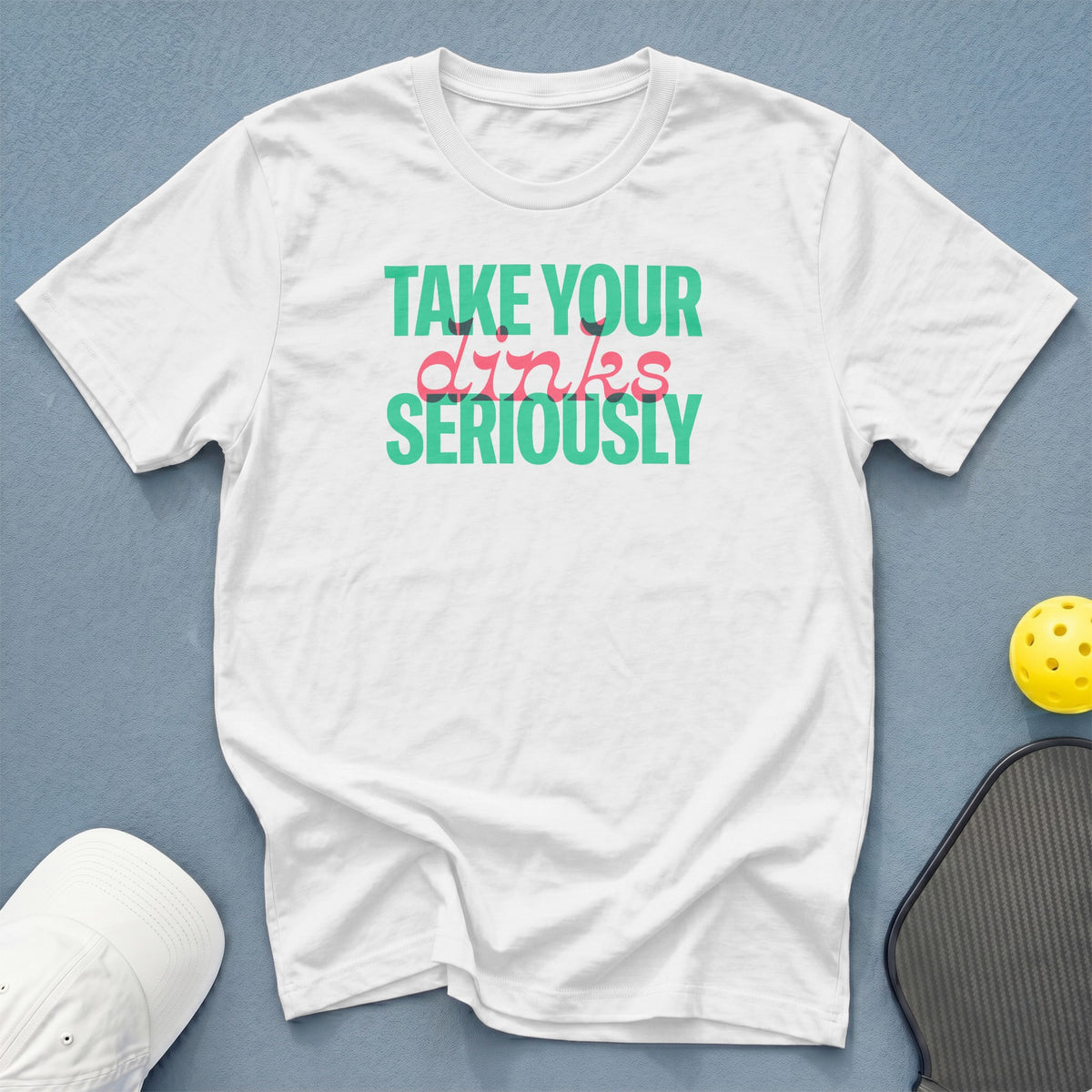 White t-shirt with "TAKE YOUR dinks SERIOUSLY" text, pickleball, and hat.