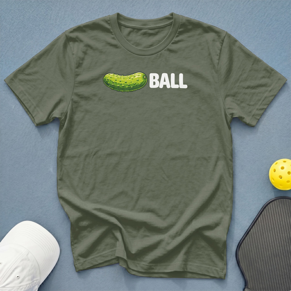 Olive t-shirt with pickle and "BALL" graphic, pickleball paddle, and ball.