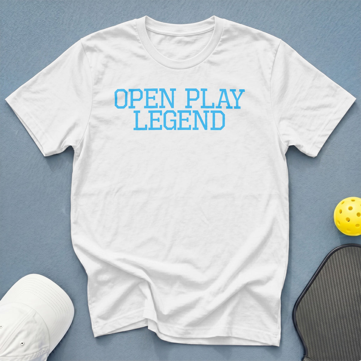 White t-shirt with blue text "OPEN PLAY LEGEND", pickleball paddle, and ball.