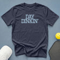 Navy t-shirt with light blue "DAY DINKIN'" text, pickleball paddle, and cap.