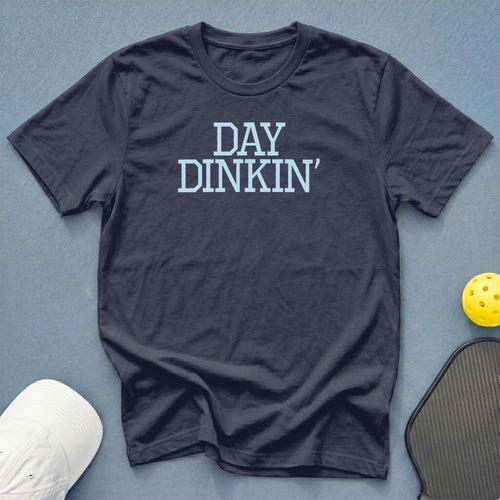 Navy t-shirt with light blue "DAY DINKIN'" text, pickleball paddle, and cap.