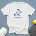 White t-shirt with blue cartoon peanut character holding a pickleball paddle and ball, text "PICKLEBALL NUT".