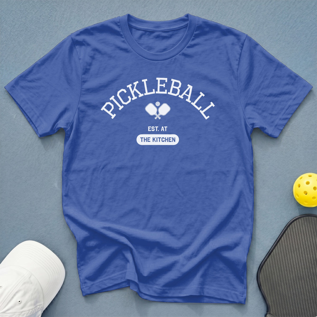 Blue t-shirt with white "Pickleball Est. At The Kitchen" graphic and pickleball paddles.