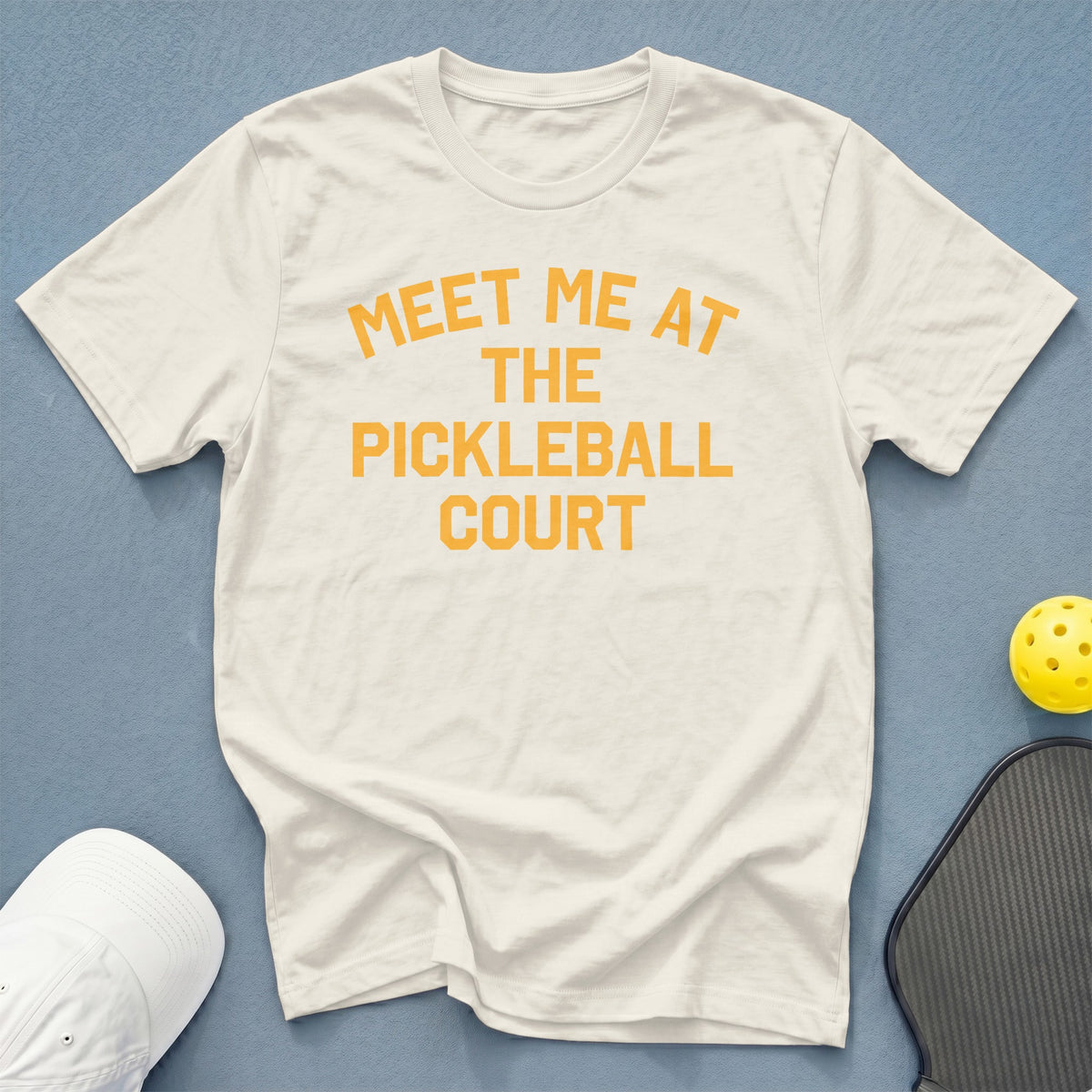White t-shirt with orange text that says "MEET ME AT THE PICKLEBALL COURT".