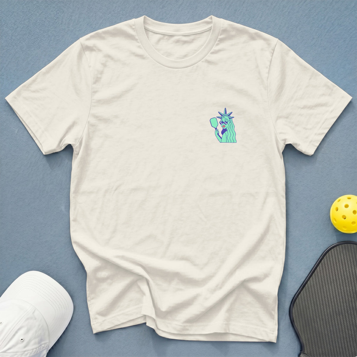 Cream t-shirt with Statue of Liberty graphic holding a pickleball paddle.