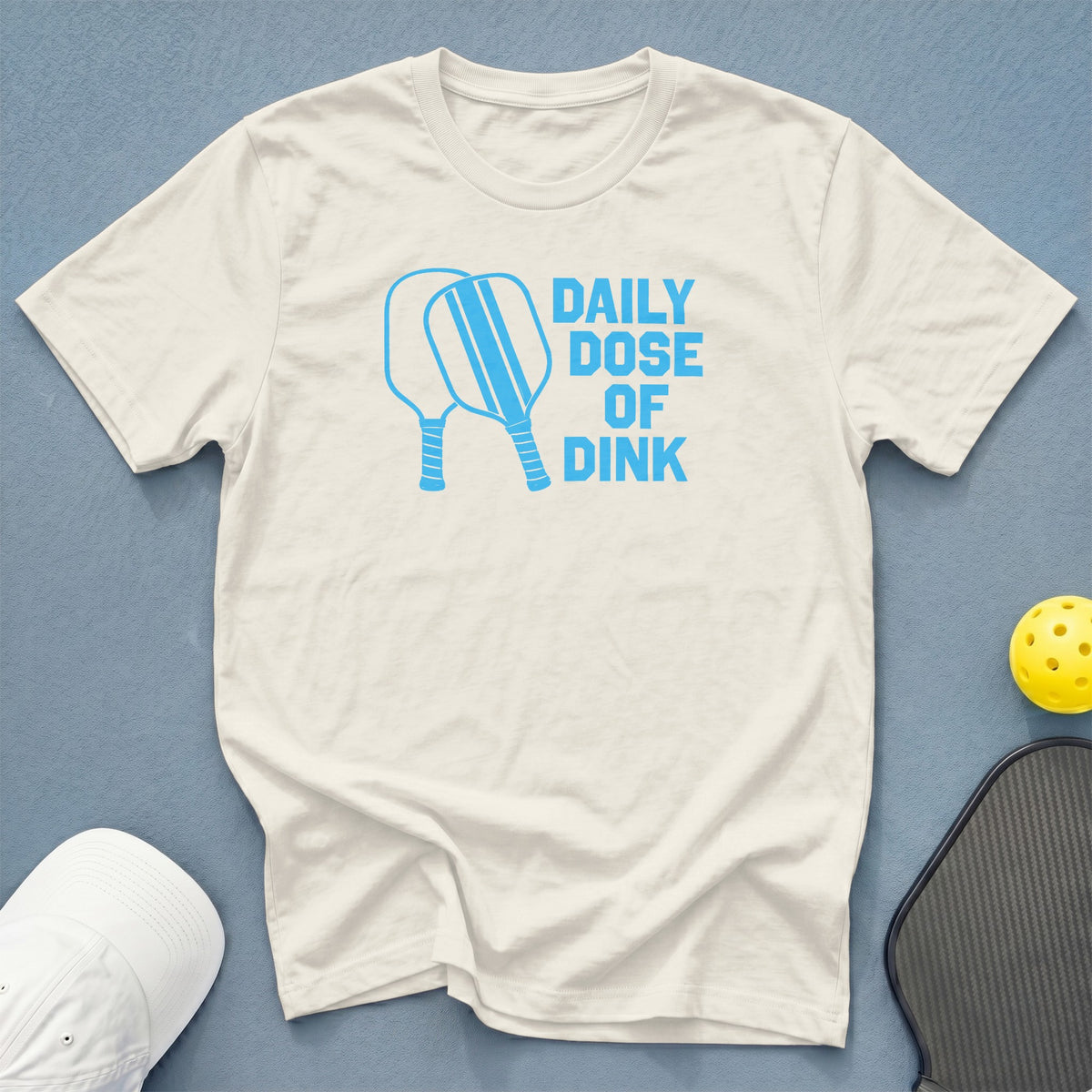 Cream t-shirt with "Daily Dose of Dink" and two pickleball paddles in blue.