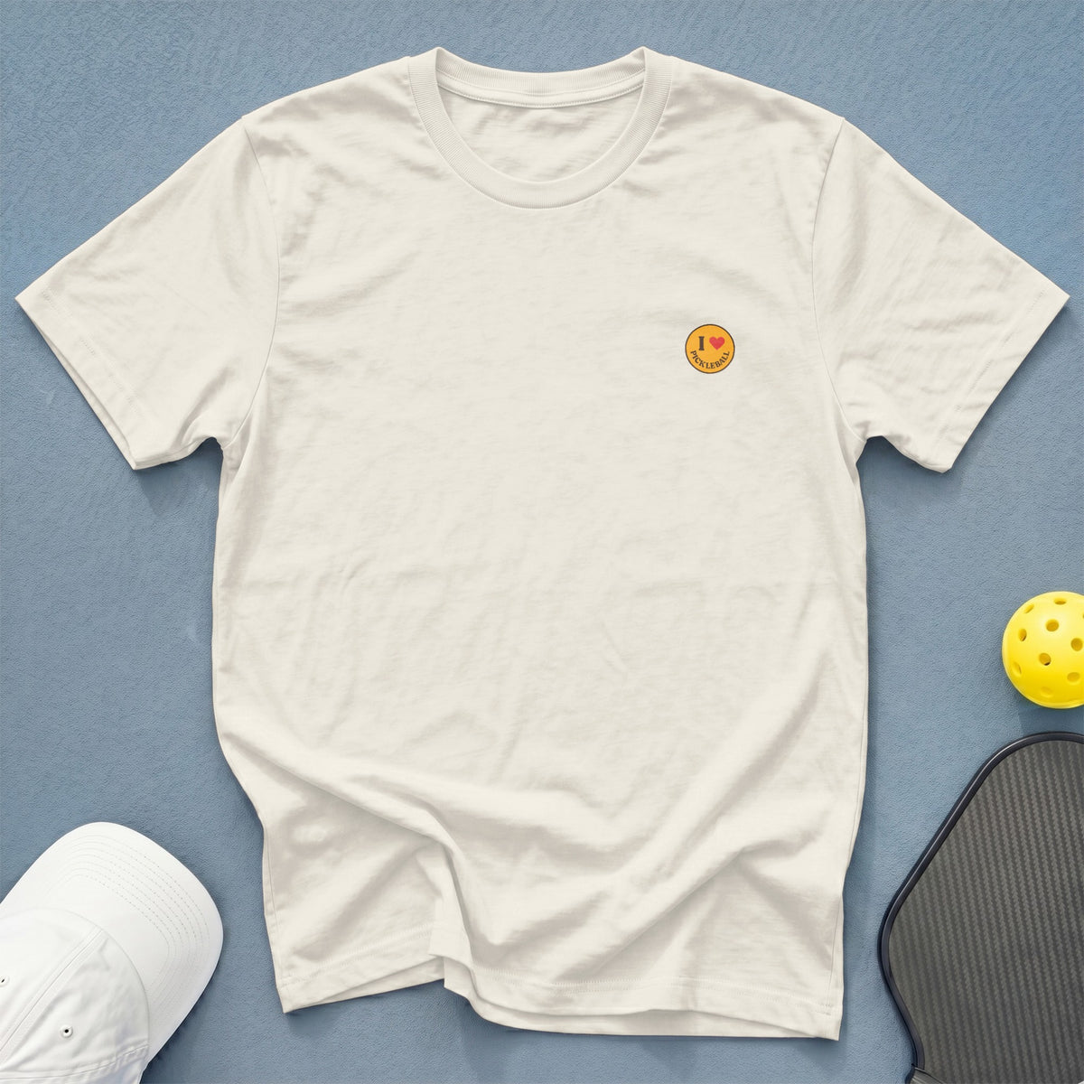 Off-white t-shirt with "I ❤️ Pickleball" graphic, white hat, and pickleball paddle.