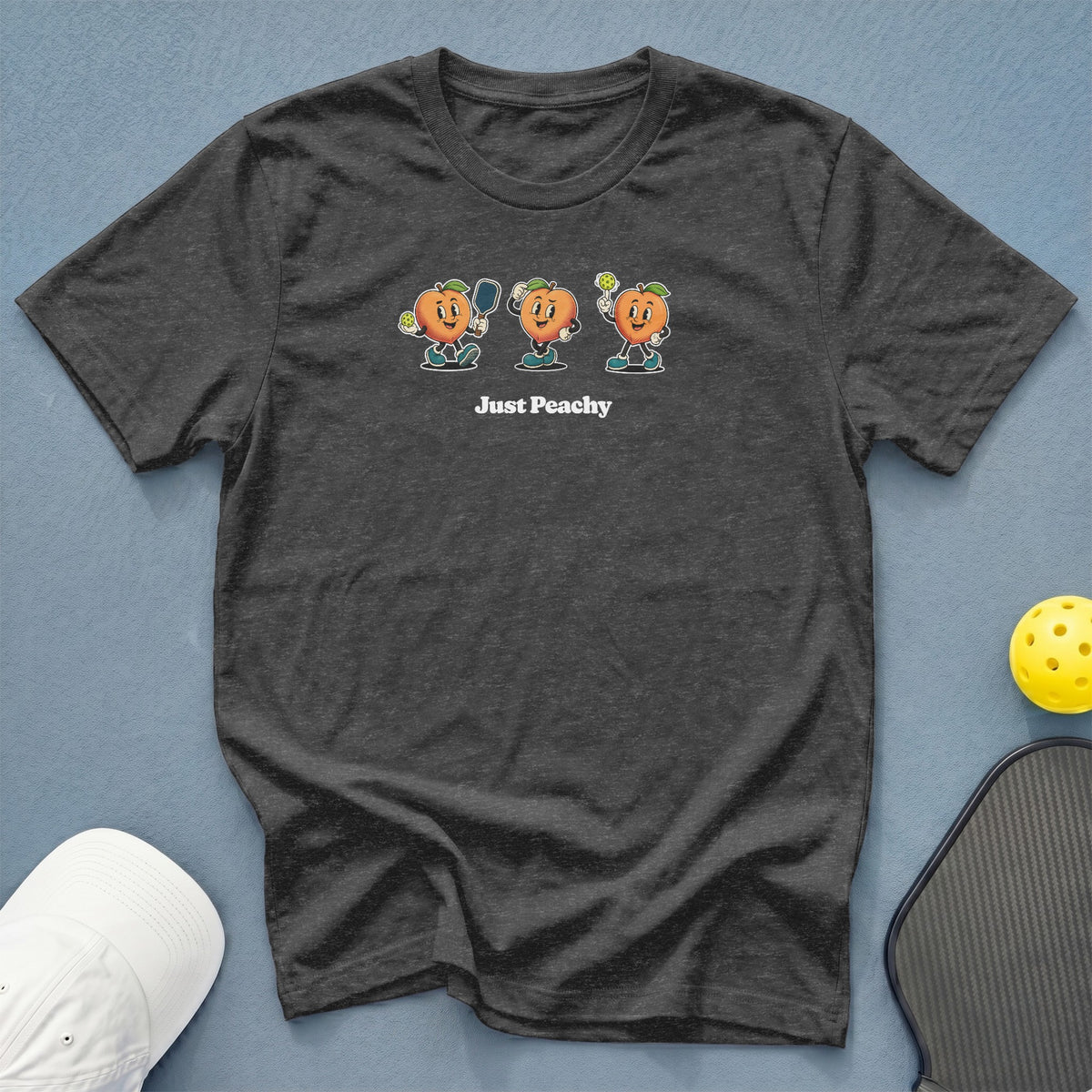 Dark grey t-shirt with three cartoon peaches playing pickleball and the text "Just Peachy".