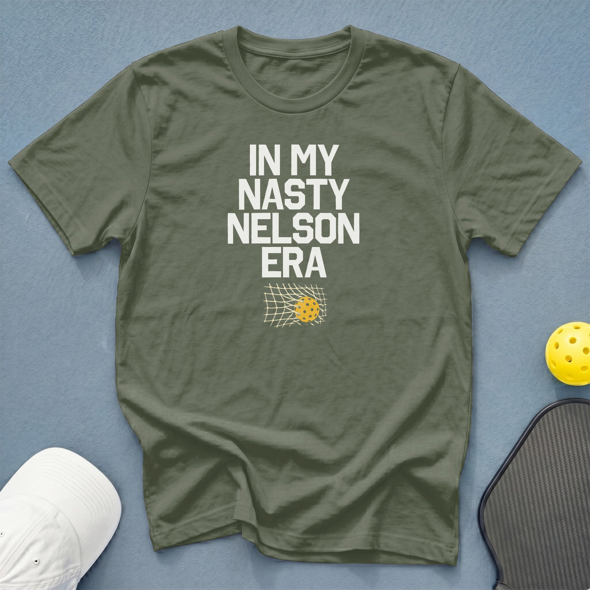 Olive green t-shirt with "In My Nasty Nelson Era" text and pickleball graphic.