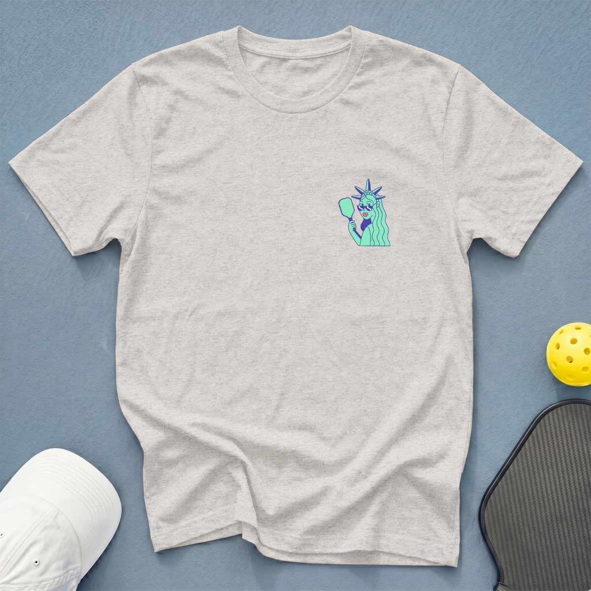 Light gray t-shirt with Statue of Liberty pickleball graphic and accessories.