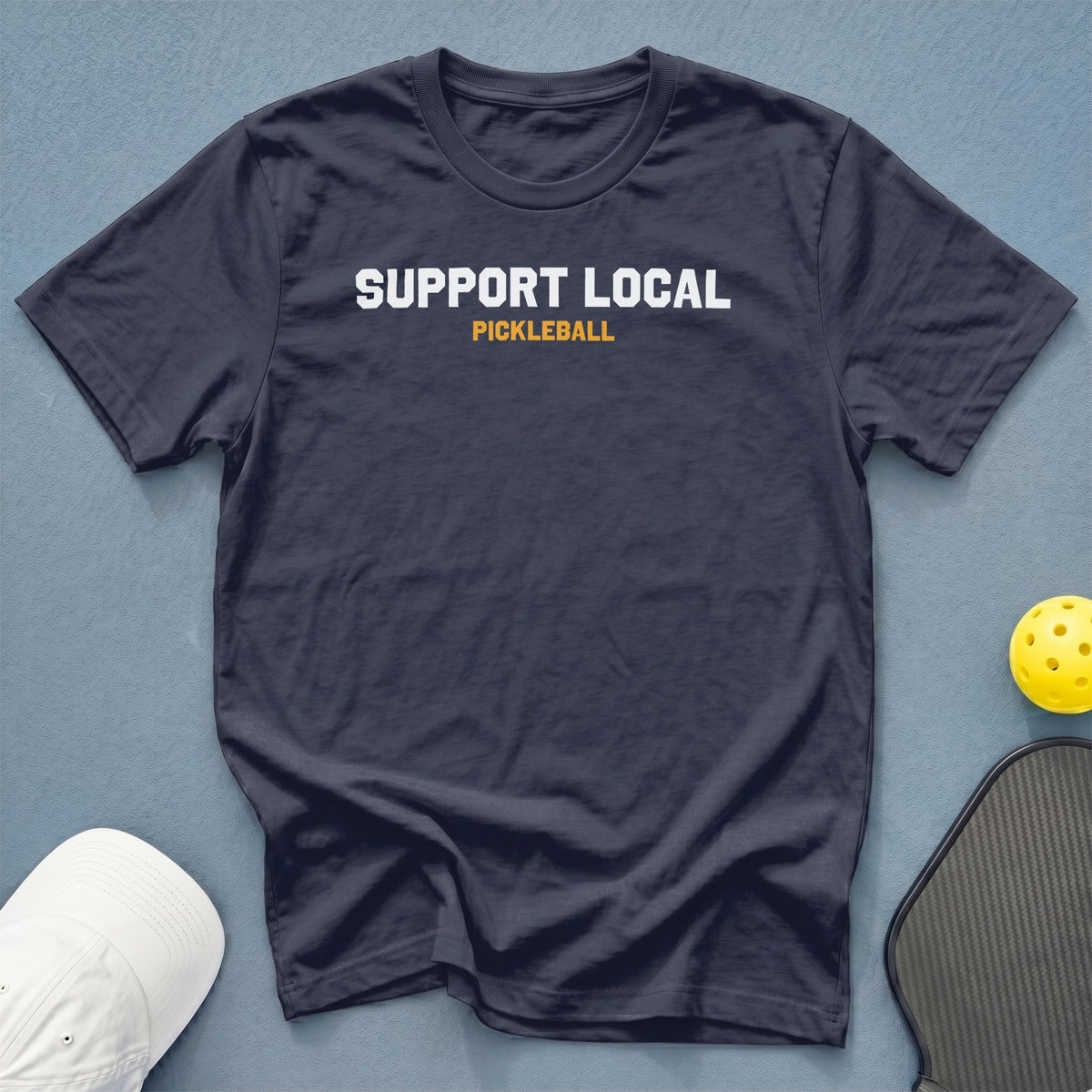 Navy t-shirt with "SUPPORT LOCAL PICKLEBALL" text, pickleball, and paddle.
