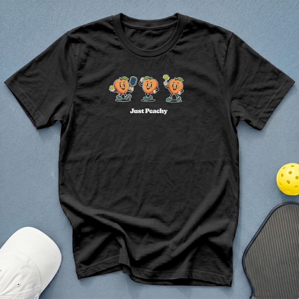 Black t-shirt with cartoon peaches playing pickleball and "Just Peachy" text.
