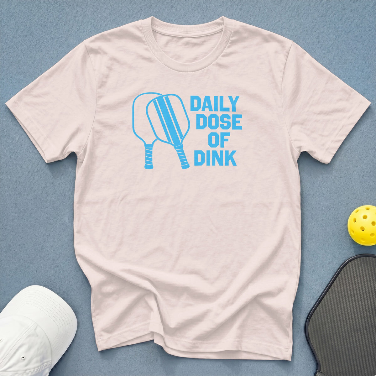 Light pink t-shirt with blue text "DAILY DOSE OF DINK" and pickleball graphics.