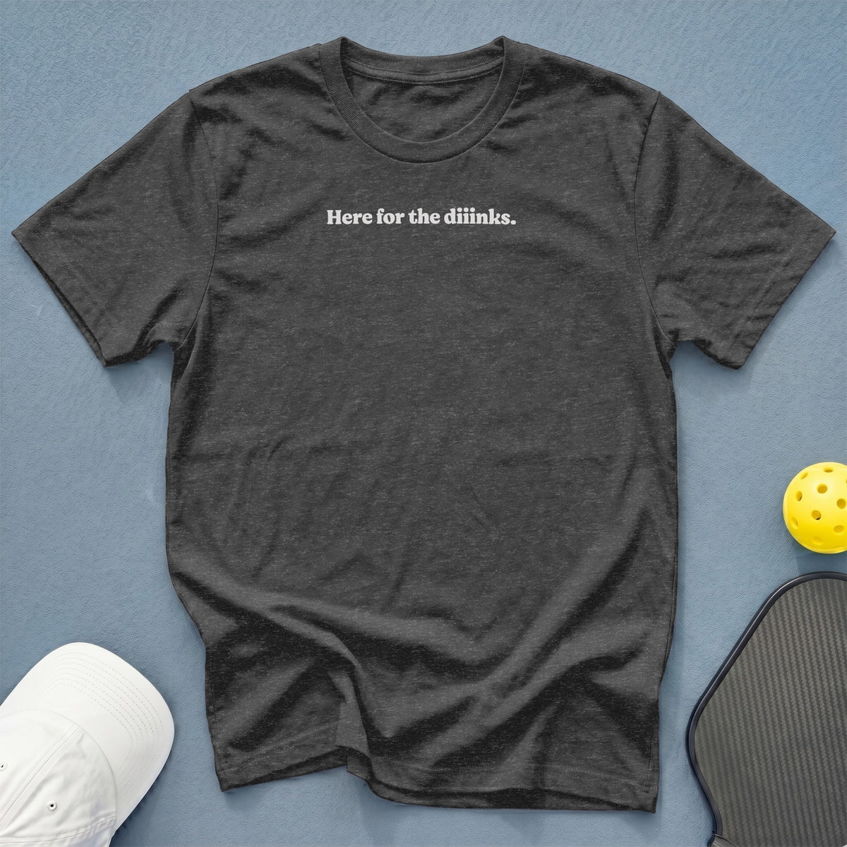 Charcoal t-shirt with white text "Here for the diinks." next to a pickleball paddle and ball.