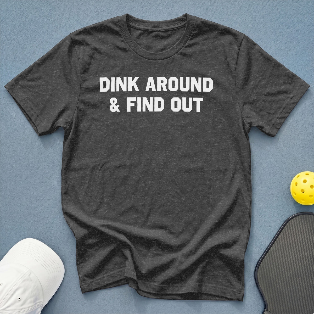 Dark gray t-shirt with white text "DINK AROUND & FIND OUT" and pickleball gear.