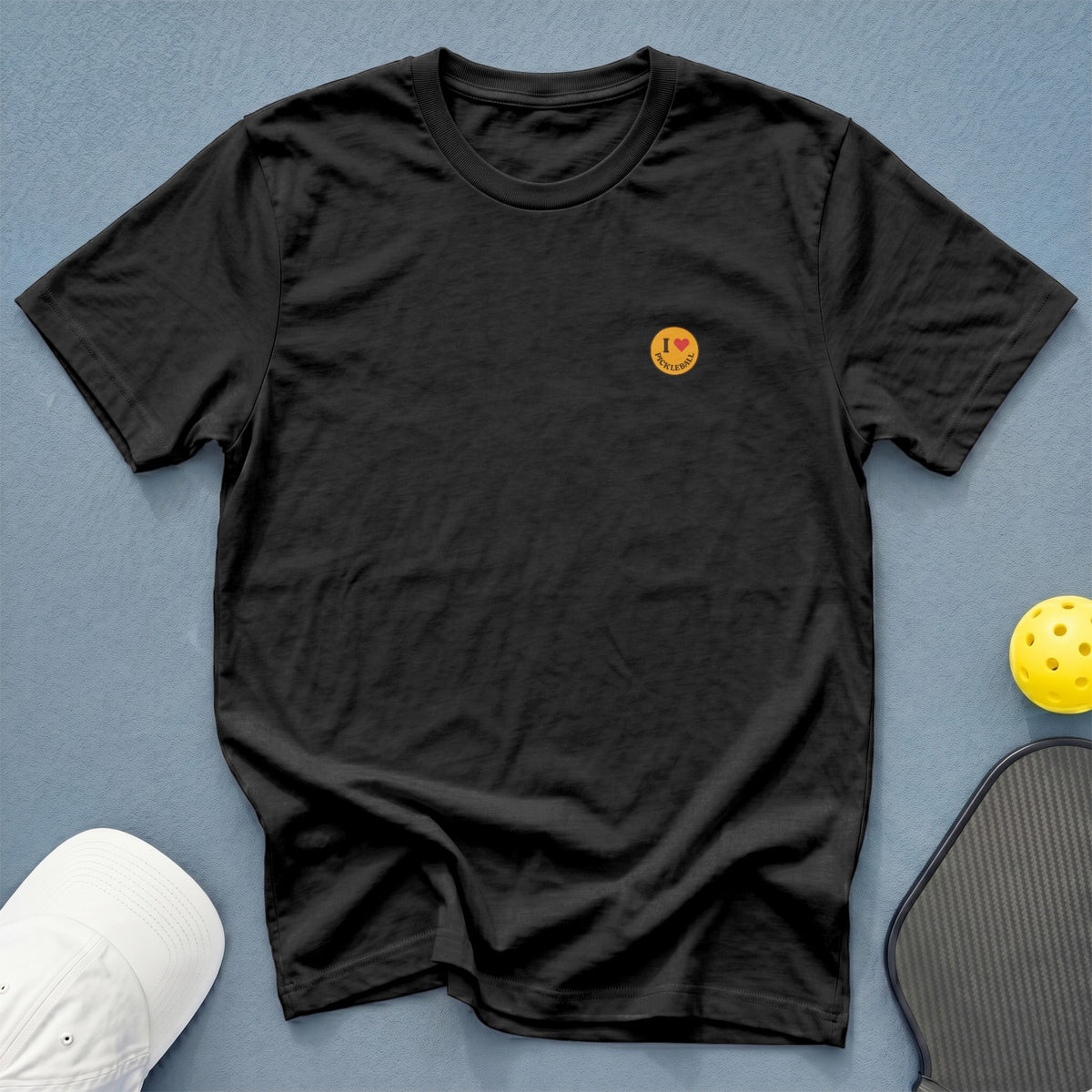 Black t-shirt with "I love pickleball" graphic on chest, next to pickleball gear.