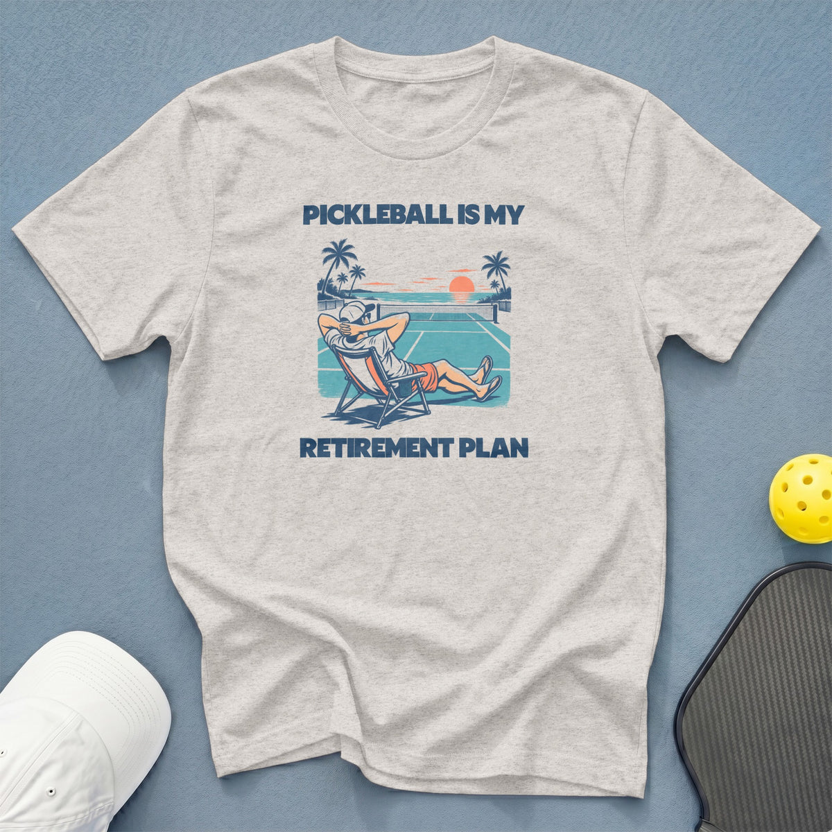 Light grey t-shirt with text "PICKLEBALL IS MY RETIREMENT PLAN" and pickleball graphic.