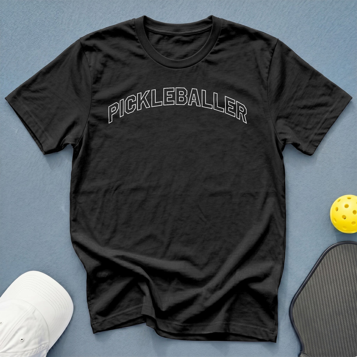 Black t-shirt with white "PICKLEBALLER" text, white hat, yellow ball, and pickleball paddle.