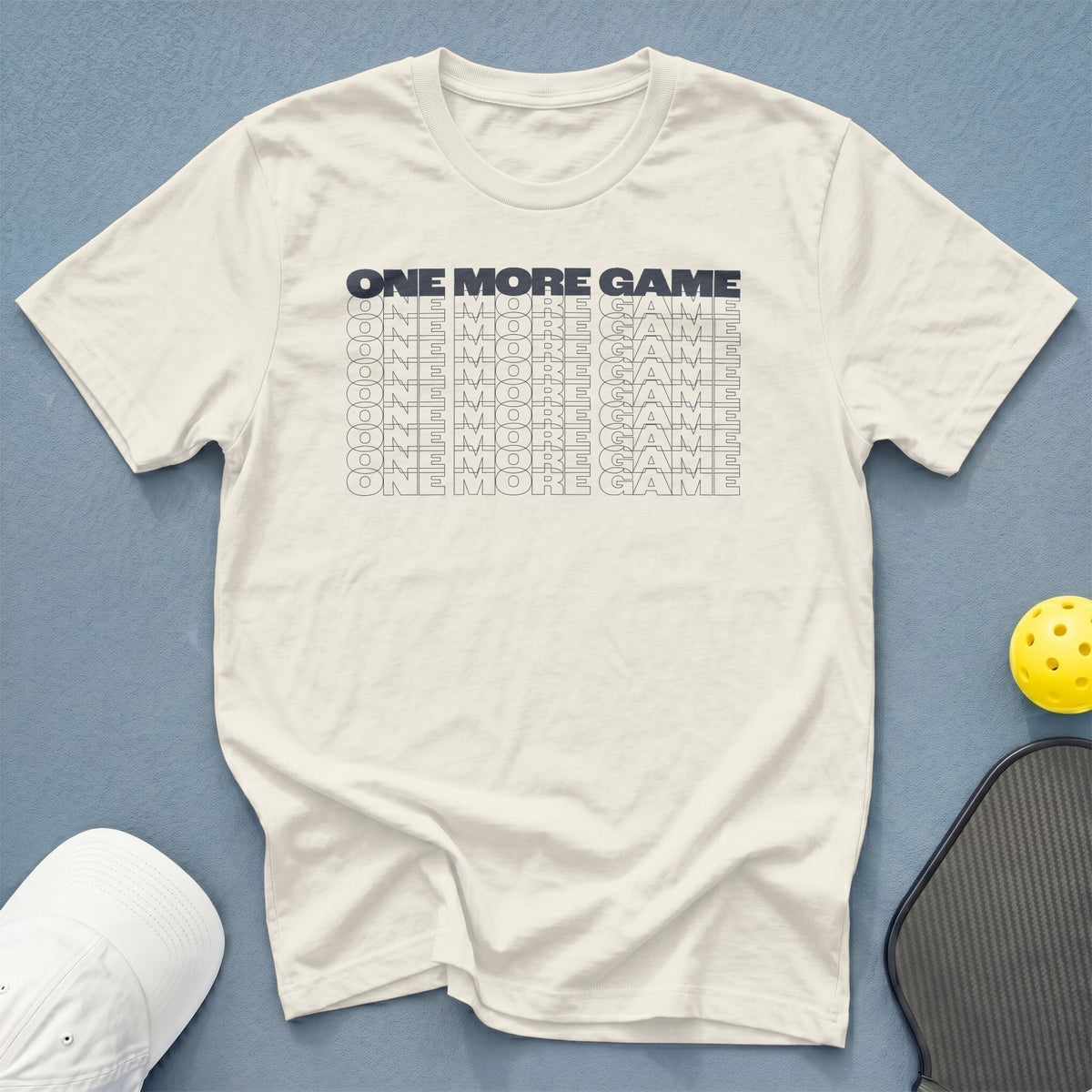 Cream t-shirt with repeated "ONE MORE GAME" text graphic.