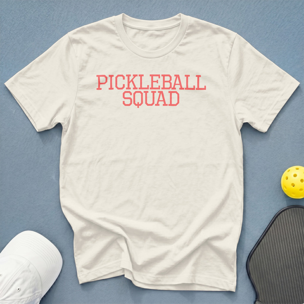 Off-white t-shirt with "PICKLEBALL SQUAD" printed in coral red.