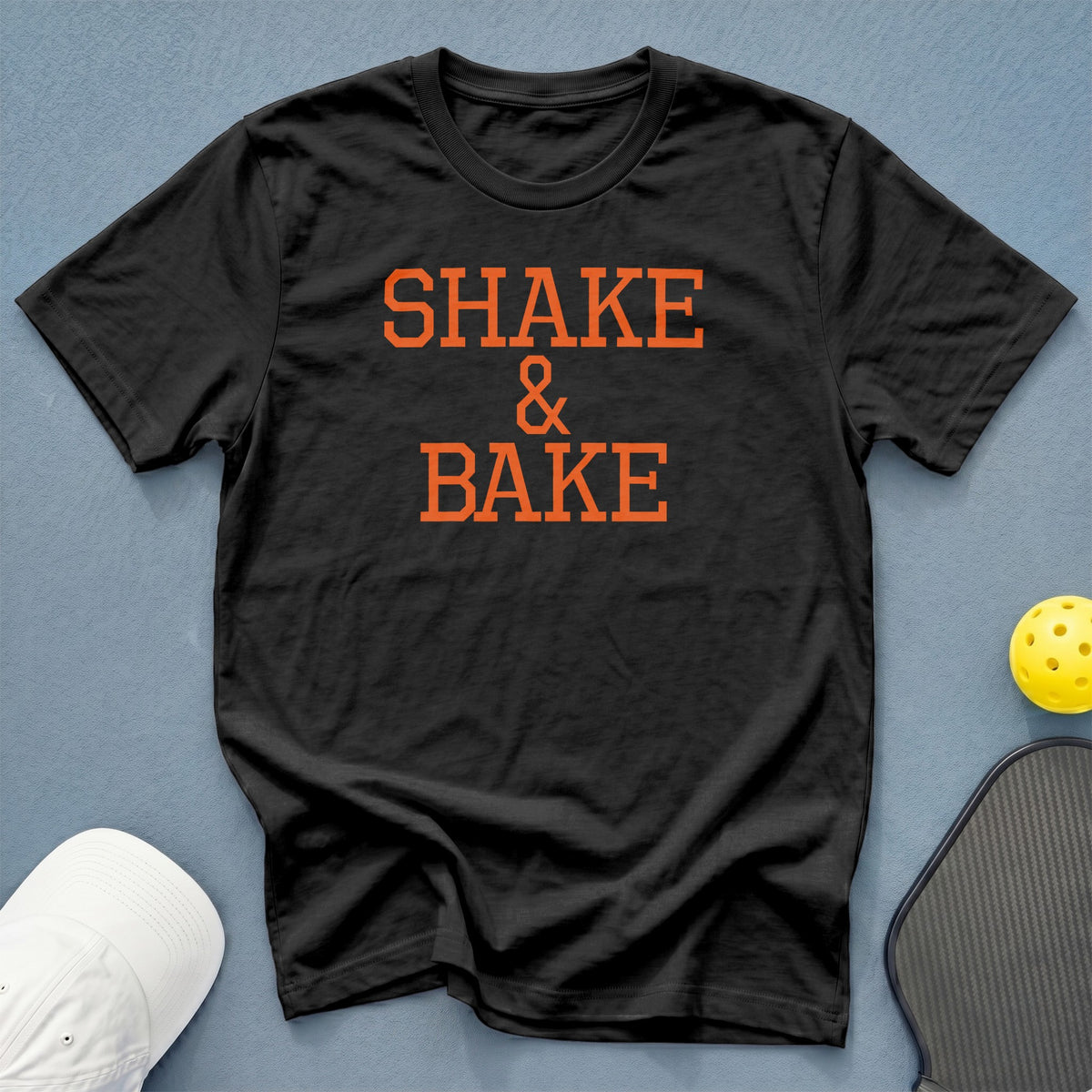 Black t-shirt with orange text "SHAKE & BAKE" and pickleball gear.